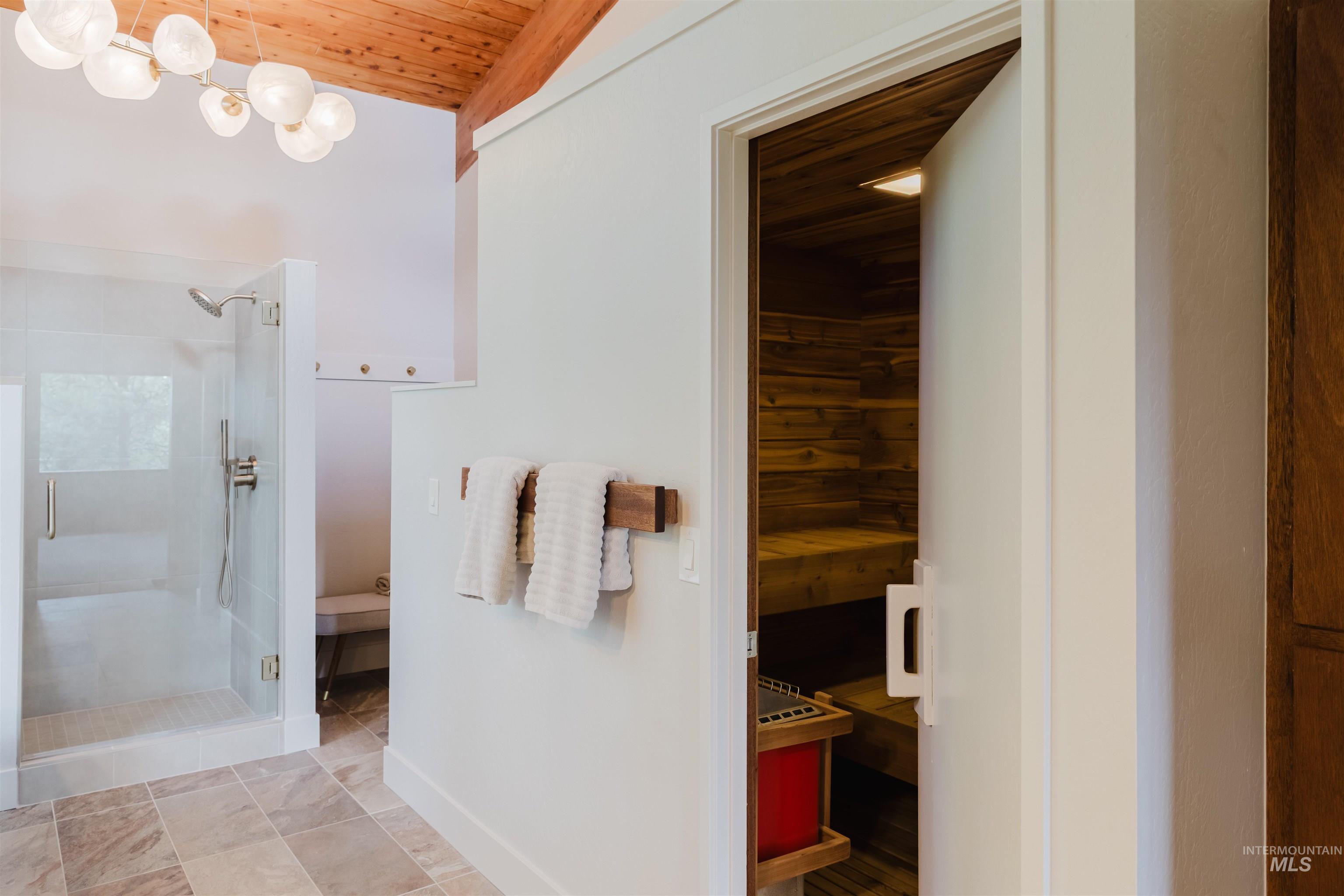 136 Silver Fox Trail McCall, ID 83638 - Photo 15 of 31 Spacious bathroom featuring a glass-enclosed shower, a sauna with wood paneling, a wood-beam ceiling, and an overhead multi-orb light fixture