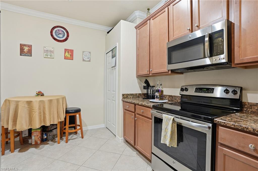 14536 Grapevine Drive Naples, FL 34114 - Photo 15 of 39 Kitchen with stainless steel appliances, ornamental molding, dark stone countertops, light tile patterned flooring, and wood finish cabinetry