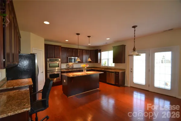 a kitchen with stainless steel appliances granite countertop a refrigerator a sink dishwasher a stove and a dining table with wooden floor