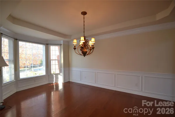 a view of an empty room with chandelier fan and wooden floor