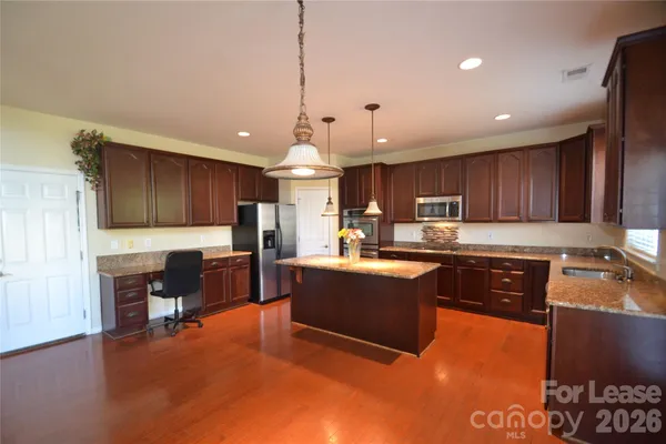 a kitchen with stainless steel appliances granite countertop a refrigerator a sink dishwasher a stove and a dining table with wooden floor