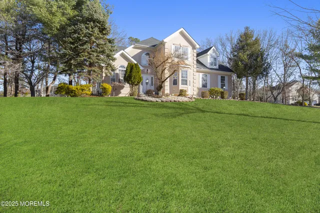 a view of a white house with a big yard and potted plants and large trees