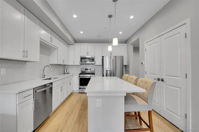 a kitchen with stainless steel appliances a stove a sink a refrigerator and white cabinets with wooden floor