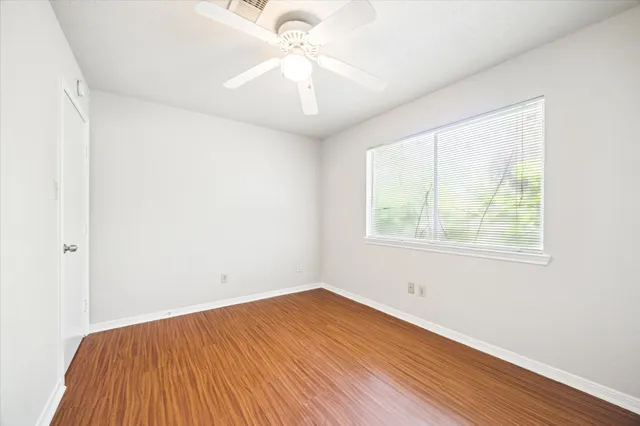 an empty room with wooden floor chandelier fan and windows