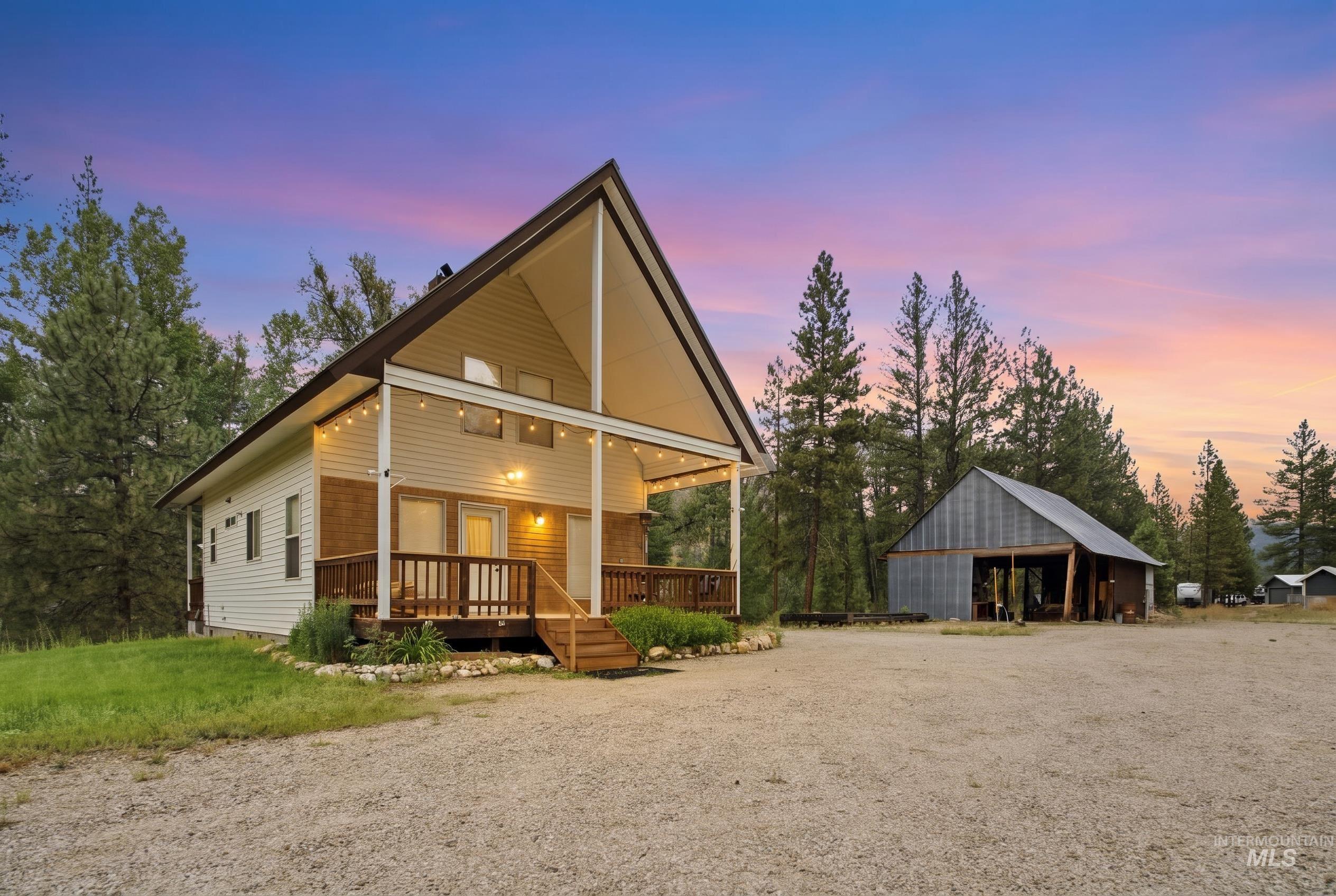 3980 North Pine-Featherville Road Mountain Home, ID 83647 - Photo 3 of 35 A-frame style residence featuring a covered porch with string lighting, wood railing, and a gravel driveway