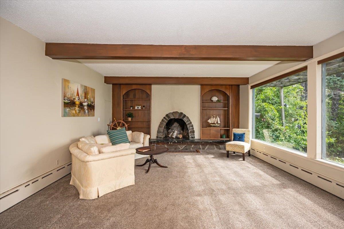 5130 London Road Duluth, MN 55804 - Photo 11 of 45 Carpeted living area featuring a baseboard heating unit, beam ceiling, a fireplace with raised hearth, a textured ceiling, and built in shelves