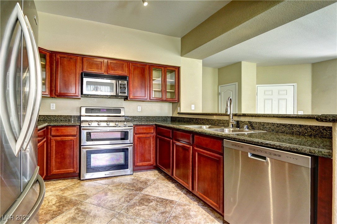 10225 King Henry Avenue, Unit 104 Las Vegas, NV 89144 - Photo 9 of 24 Kitchen featuring dark brown cabinets, glass insert cabinets, stainless steel appliances, and dark stone countertops