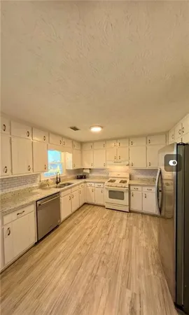 a large kitchen with a large counter top a sink stainless steel appliances and cabinets