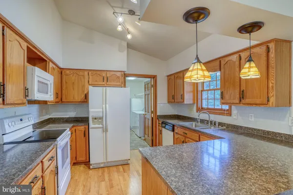a kitchen with stainless steel appliances granite countertop a refrigerator a sink dishwasher a stove and a dining table with wooden floor
