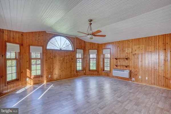 an empty room with wooden floor fan and windows