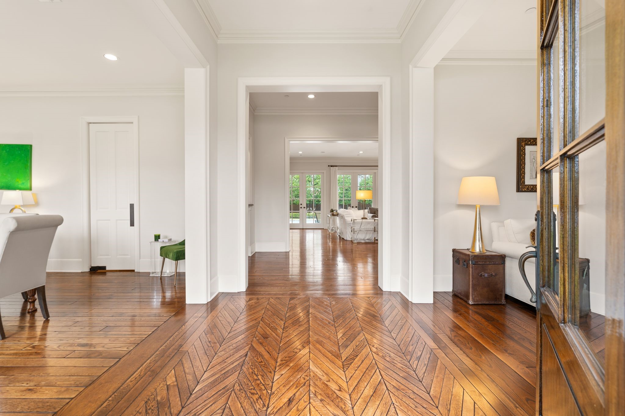11402 Taylorcrest Road Houston, TX 77024 - Photo 6 of 44 Elegant entry framed by a mahogany front door with privacy shade, sets a warm and refined first impression. Striking herringbone-pattern hardwood floors anchor the space, complemented by crown molding, cased openings, recessed lighting, and approx. 11’ ceiling height. A timeless introduction to the home’s thoughtful architectural design.