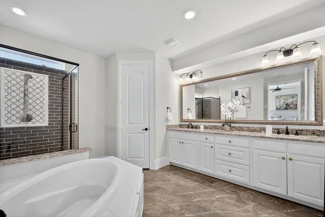 a bathroom with a granite countertop double vanity sink a mirror and a bathtub