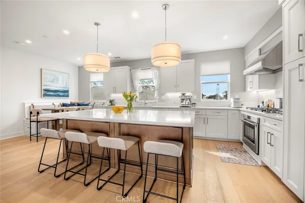 a kitchen with stainless steel appliances kitchen island granite countertop a sink a stove a dining table and chairs with wooden floor