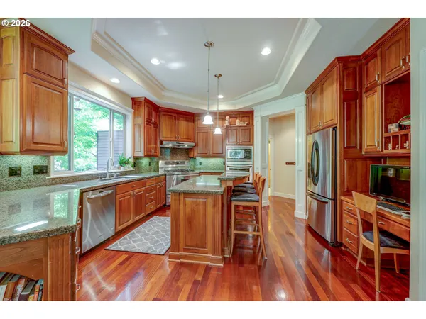 a kitchen with stainless steel appliances granite countertop a refrigerator a sink dishwasher a stove and a dining table with wooden floor