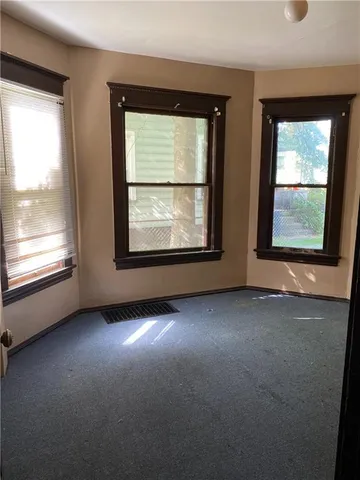 an empty room with windows and view of kitchen