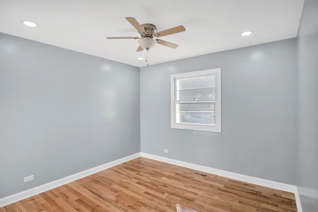 an empty room with wooden floor fan and windows