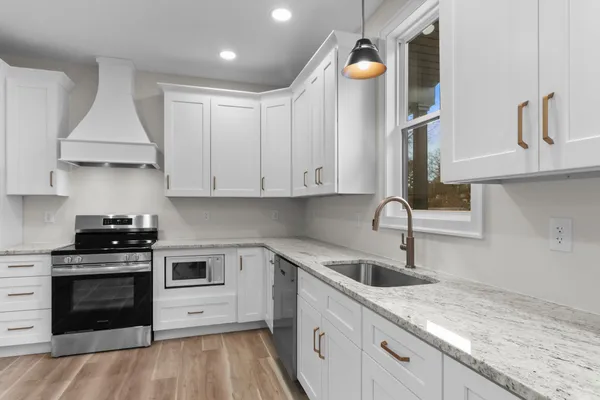 a kitchen with granite countertop a stove a sink and a white cabinets