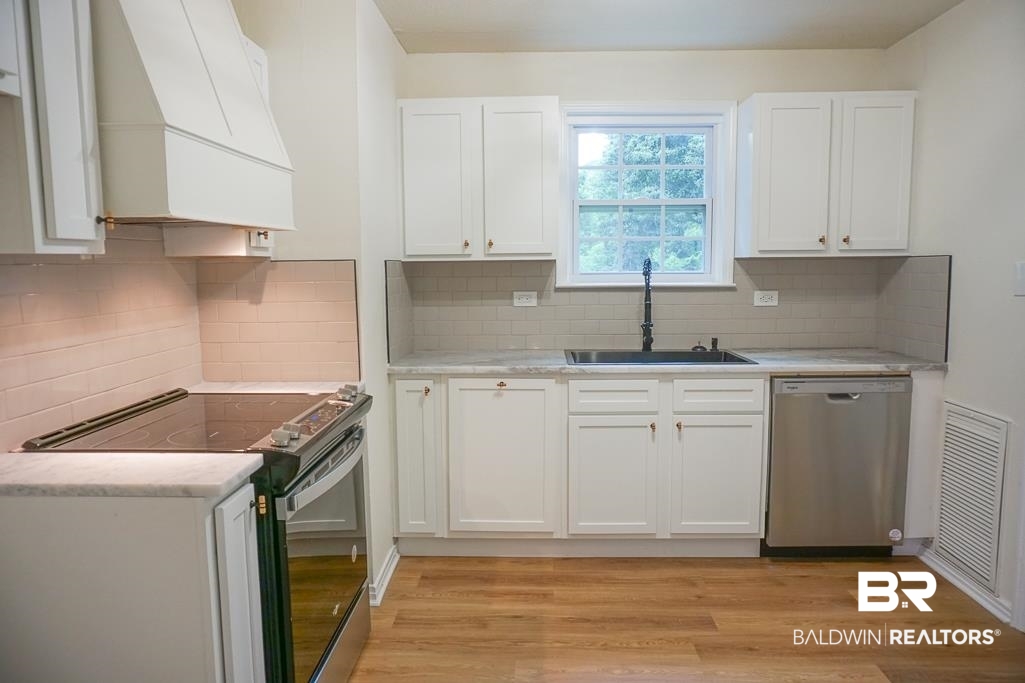 4734 Kirkwell Drive Mobile, AL 36619 - Photo 6 of 18 Kitchen with light hardwood / wood-style flooring, premium range hood, stainless steel appliances, sink, and white cabinets