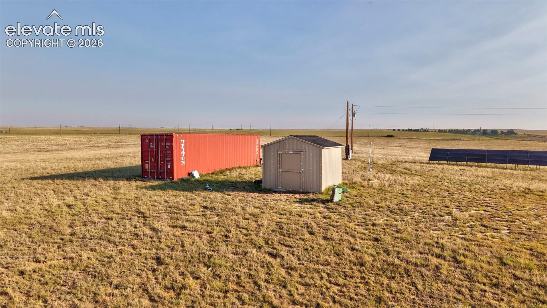 9670 Boone Road Yoder, CO 80864 - Photo 11 of 17 Expansive property featuring a red shipping container, a compact storage shed with a dark roof, and a ground-mounted solar panel array
