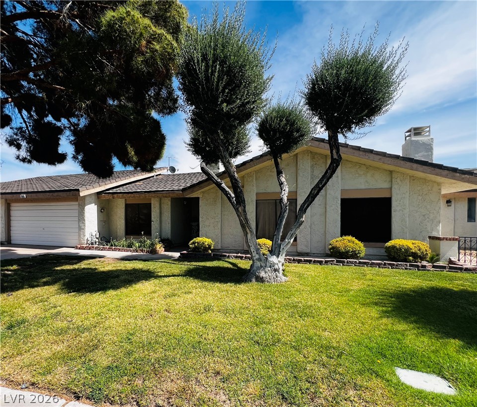 View of front of property featuring a garage, stucco siding, a front lawn, a chimney, and concrete driveway