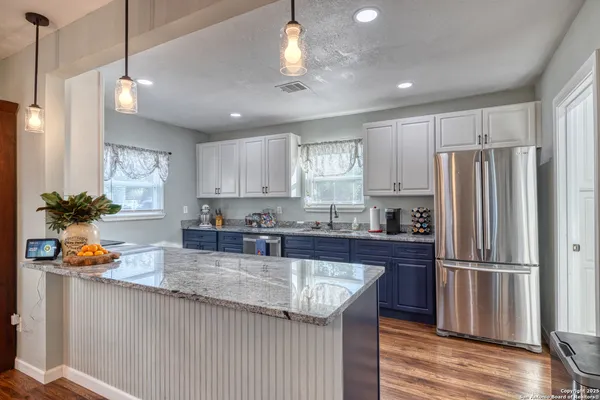 a kitchen with stainless steel appliances granite countertop a refrigerator a sink dishwasher a stove and white cabinets with wooden floor