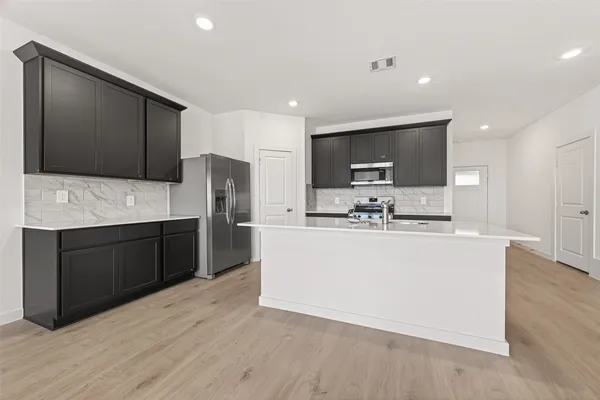 a large kitchen with stainless steel appliances a large counter top a stove a microwave a sink and cabinets