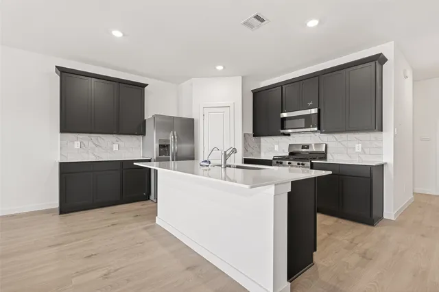 a large kitchen with stainless steel appliances a large counter top a stove a microwave a sink and cabinets