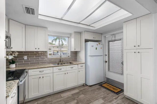 a kitchen with stainless steel appliances kitchen island granite countertop a refrigerator a sink dishwasher a dining table and chairs with wooden floor