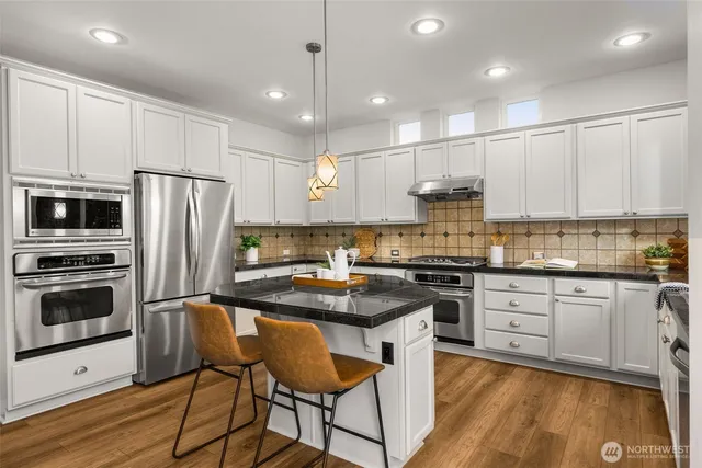 a kitchen with stainless steel appliances granite countertop a stove a sink dishwasher a refrigerator and white cabinets with wooden floor