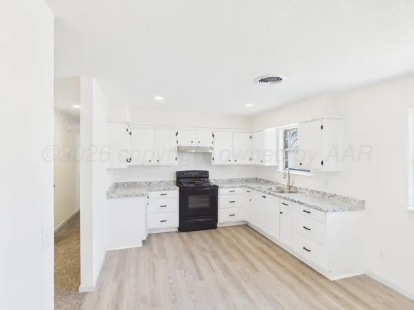 a large white kitchen with a stove a sink dishwasher and a refrigerator with white cabinets