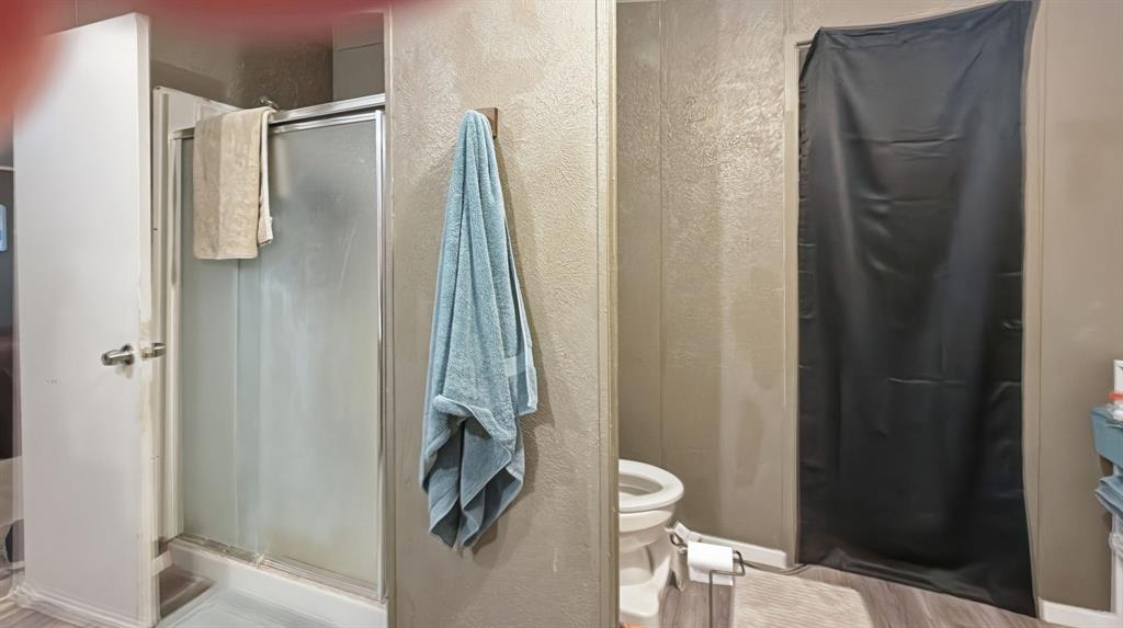 185 Private Road 4437 Rhome, TX 76078 - Photo 11 of 28 Enclosed shower with frosted glass doors and a white base, complemented by light-toned wall paneling and wood-finish flooring