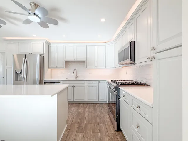 a kitchen with stainless steel appliances white cabinets a sink a stove a refrigerator and island with wooden floor