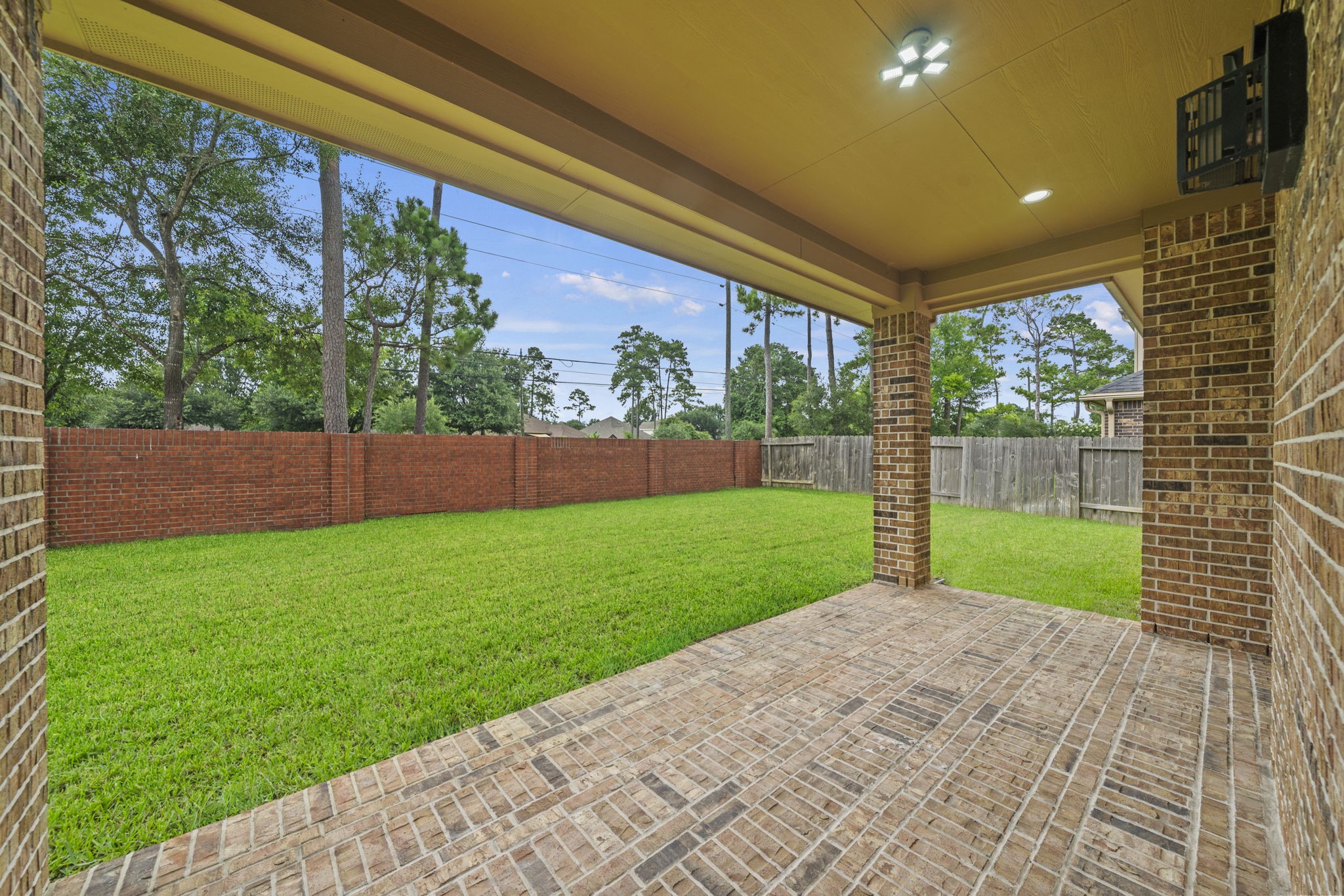14215 Spindle Arbor Road Cypress, TX 77429 - Photo 41 of 47 This photo showcases a spacious covered patio with brick flooring, overlooking a large, well-maintained grassy backyard. The area is enclosed by a combination of wooden and brick fencing, providing privacy and a serene view of surrounding trees. Perfect for outdoor relaxation and entertainment.