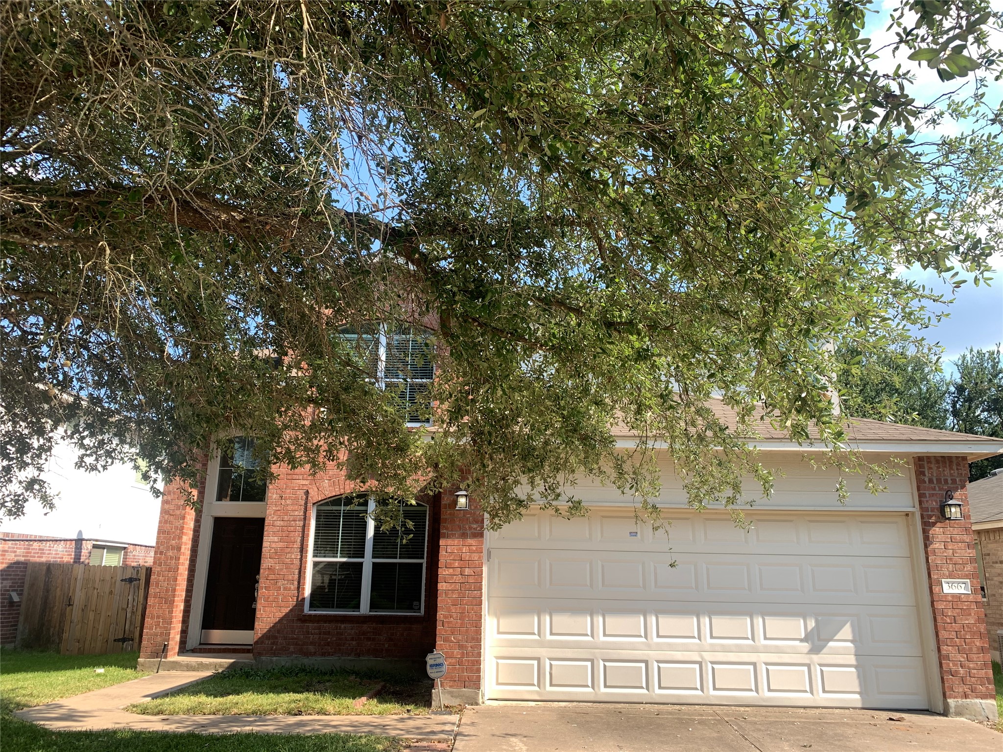 View of property hidden behind natural elements featuring brick siding and concrete driveway