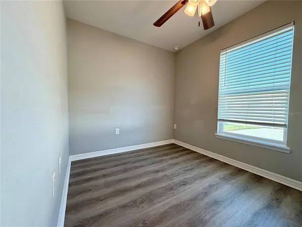 an empty room with wooden floor chandelier fan and windows