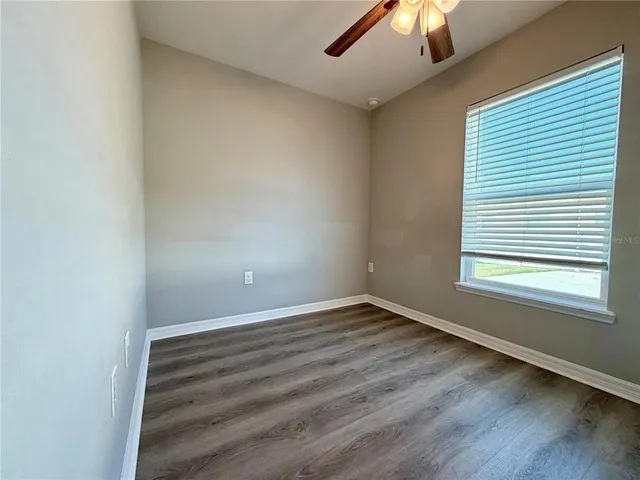 an empty room with wooden floor chandelier fan and windows
