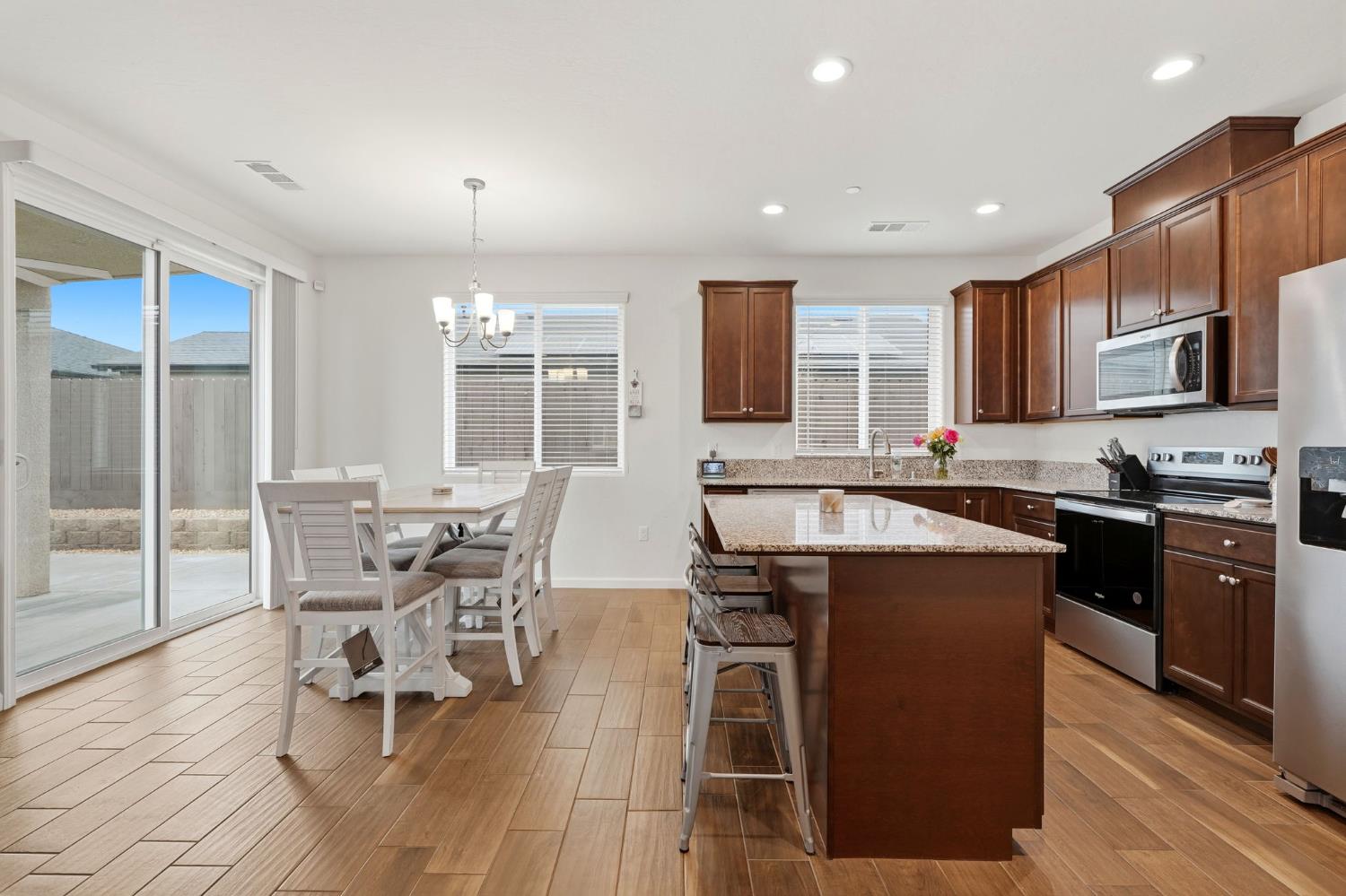 3125 Seymour Street Tulare, CA 93274 - Photo 16 of 52 a kitchen with stainless steel appliances granite countertop a stove top oven a sink dishwasher a dining table and chairs with wooden floor