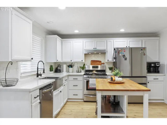 a kitchen with stainless steel appliances a stove a sink a refrigerator white cabinets and wooden floor