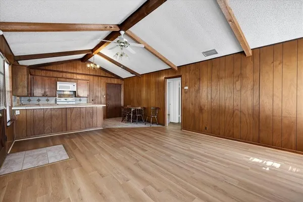 an empty room with wooden floor and way to kitchen
