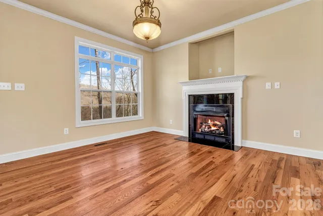 a view of an empty room with wooden floor fireplace and a window