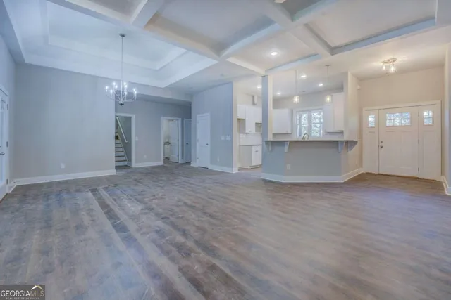 an empty room with wooden floor and kitchen view