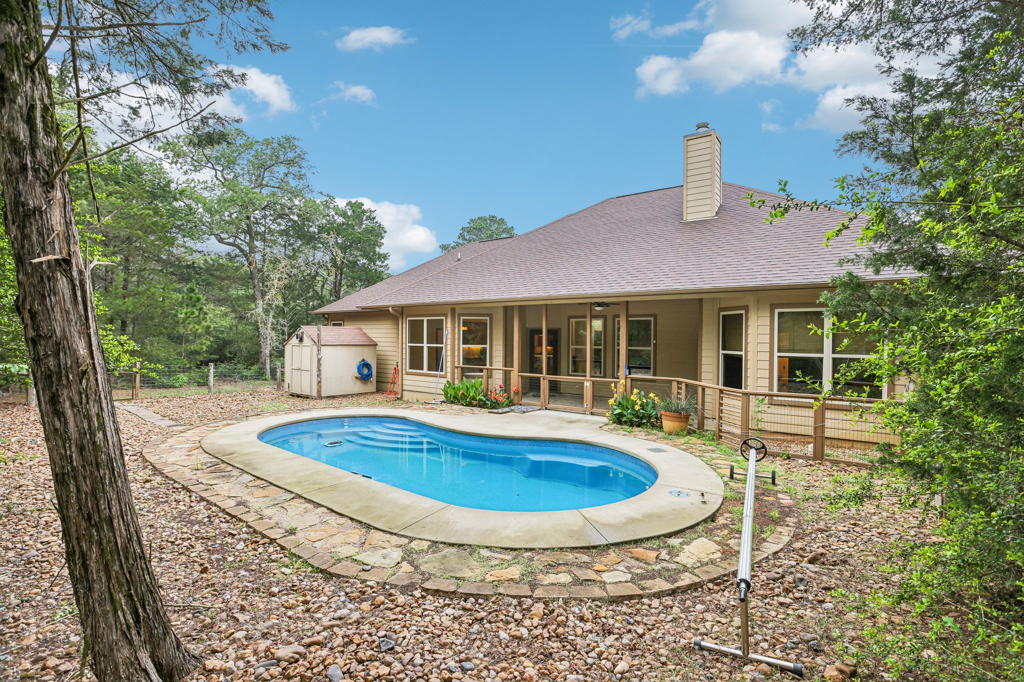 267 Corral Road Smithville, TX 78957 - Photo 36 of 40 Backyard featuring a freeform swimming pool with stone coping, a surrounding stone pathway, and a detached storage shed