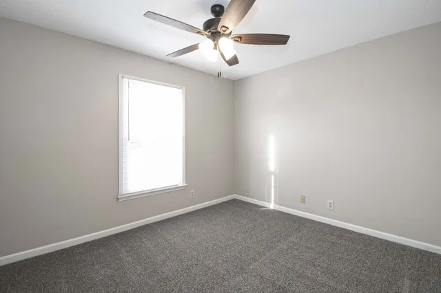 an empty room with chandelier fan and windows
