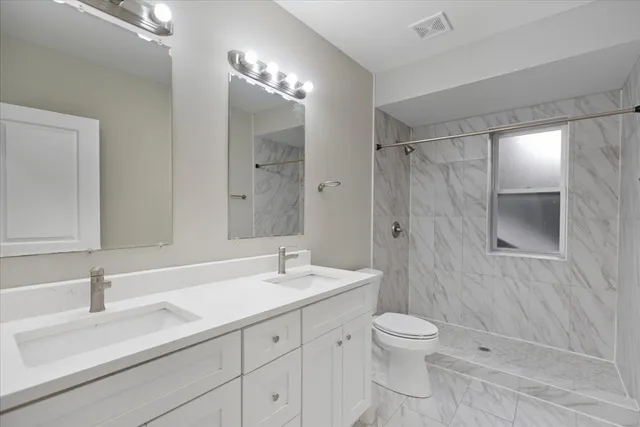 a bathroom with a toilet a double vanity sink and mirror
