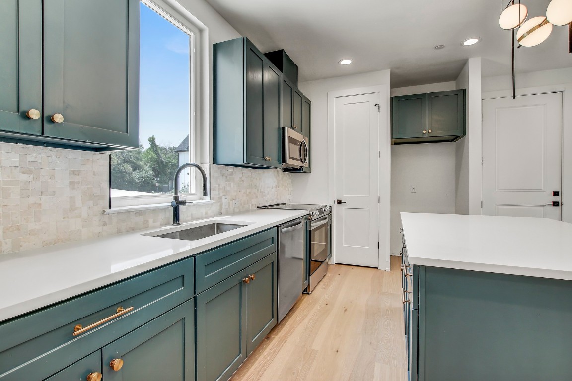 4127 East 12th Street, Unit 5 Austin, TX 78721 - Photo 3 of 33 Kitchen with a sink, appliances with stainless steel finishes, light wood-style floors, tasteful backsplash, and recessed lighting