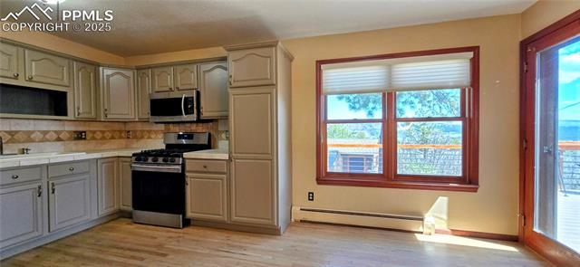 18170 Forest View Road Monument, CO 80132 - Photo 5 of 32 Kitchen with stainless steel appliances, a baseboard heating unit, a sink, decorative backsplash, and light wood finished floors