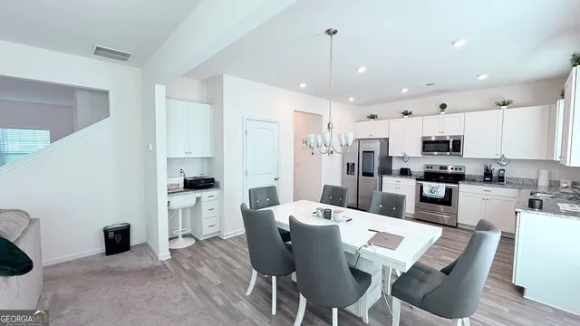 a kitchen with stainless steel appliances kitchen island granite countertop a refrigerator a stove a sink a dining table and chairs with wooden floor