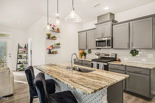 a kitchen with stainless steel appliances granite countertop a stove top oven a sink a dining table and chairs with wooden floor