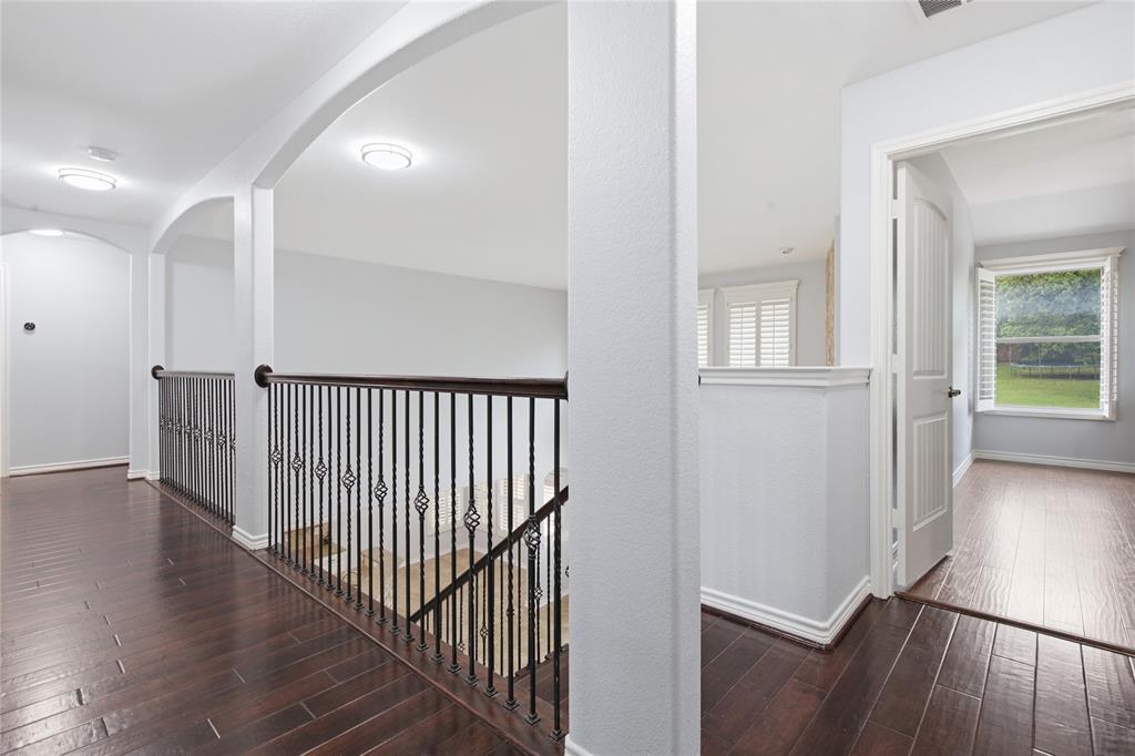 10001 Thurman Road Fort Worth, TX 76244 - Photo 21 of 40 Upper-level hallway featuring dark wood-finish flooring, white walls, arched doorways, and ornate black iron balusters