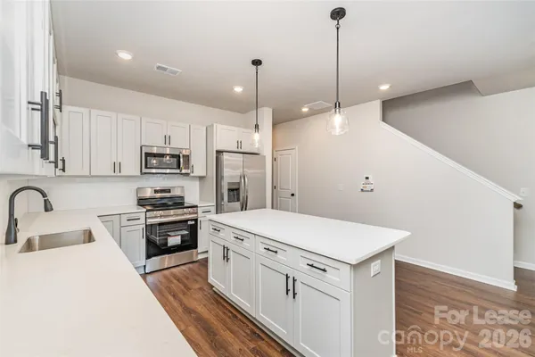 a kitchen with stainless steel appliances a stove a sink dishwasher a refrigerator white cabinets and wooden floor